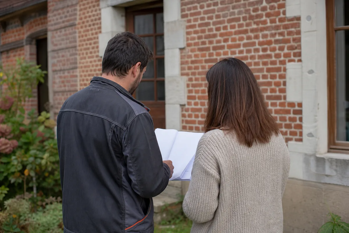 Artisan et particulier comparant des devis de chauffage devant un logement ancien